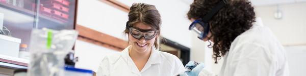 两名女学生穿着磨砂膏和防护眼镜在化学实验室里.